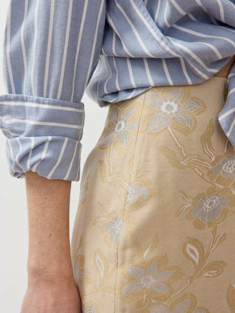 Beige pencil skirt with subtle floral embroidery paired with blue and white striped shirt.