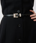 Black leather belt with rectangular gold buckle worn over black buttoned dress.