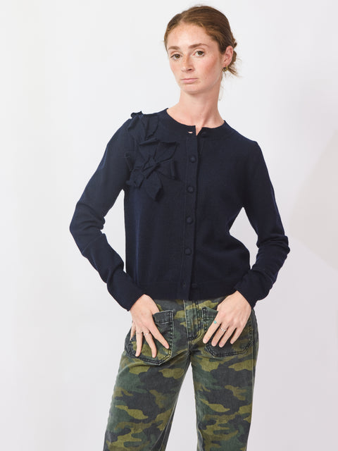 Woman wearing a navy blue blouse with ruffles and camouflage pants on a white background