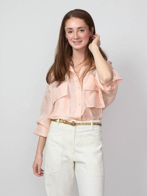 smiling woman wears a blush pink silk button down shirt with white denim pants.