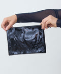 Person holding a black textured pouch against a light gray background