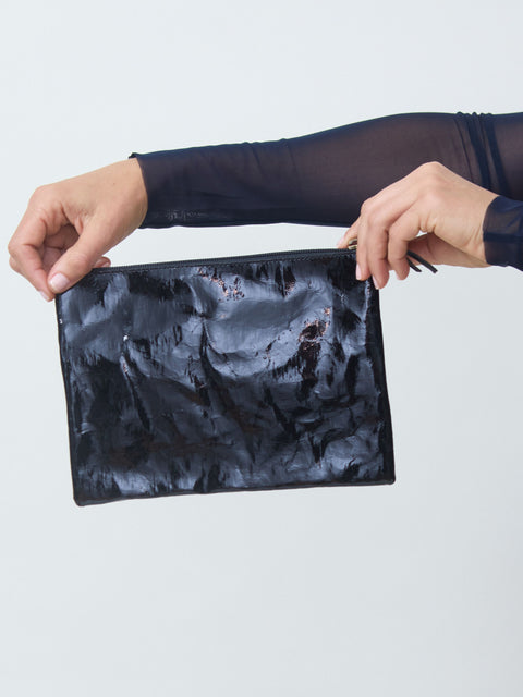 Person holding a black textured pouch against a light gray background