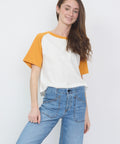 White and mustard yellow baseball tee with short sleeves paired with blue jeans.