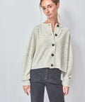 Woman wearing a light-colored cardigan with button details on a plain background