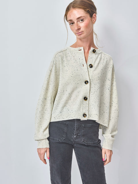 Woman wearing a light-colored cardigan with button details on a plain background