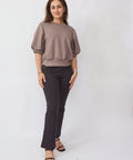 Woman wearing a brown top and black pants on a white background