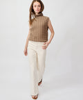 Woman wearing a sleeveless beige cable-knit turtleneck sweater and high-waisted bone-colored wide-leg pants.