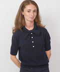 Woman wearing a navy blue blouse with a large collar and buttons on a white background