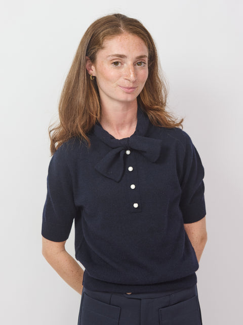 Woman wearing a navy blue blouse with a large collar and buttons on a white background
