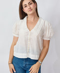 Woman wearing a white blouse with short sleeves and blue jeans on a plain background