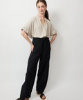 Black high-waist relaxed fit pants with gathered elastic waistband worn with beige short-sleeve blouse and sandals.