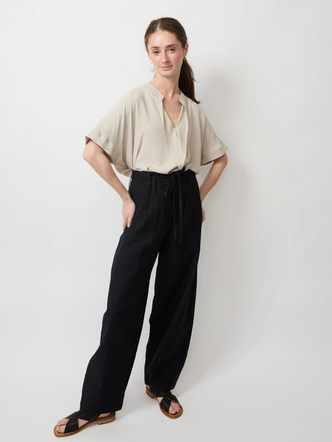 Black high-waist relaxed fit pants with gathered elastic waistband worn with beige short-sleeve blouse and sandals.
