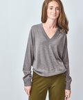 Woman wearing a gray sweater and green pants on a light gray background