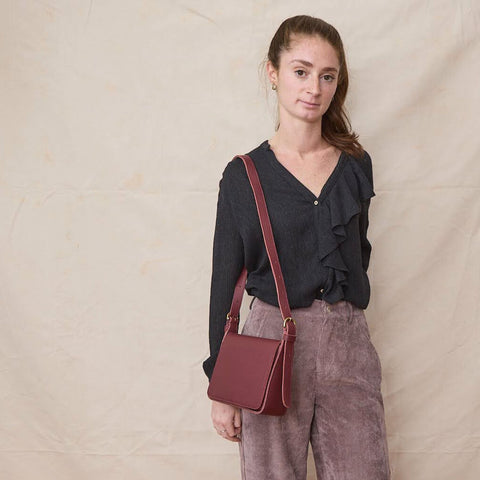 Young woman wears a black blouse with front ruffles, corduroy trousers and a burgundy crossbody leather bag