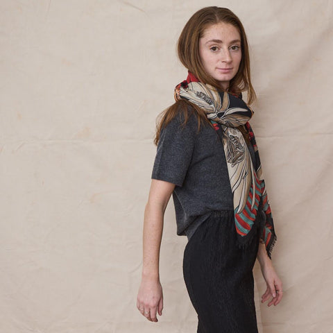 Young woman wears a grey cashmere tee, black pants and a tan/red wool scarf.