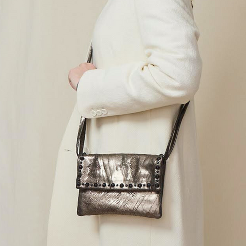 Woman wears a cream coat and holds a metallic silver crossbody bag