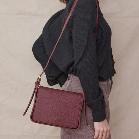 Woman wears a dark grey long sleeve top with wide leg corduroy pants and carries a  burgundy leather messenger bag 