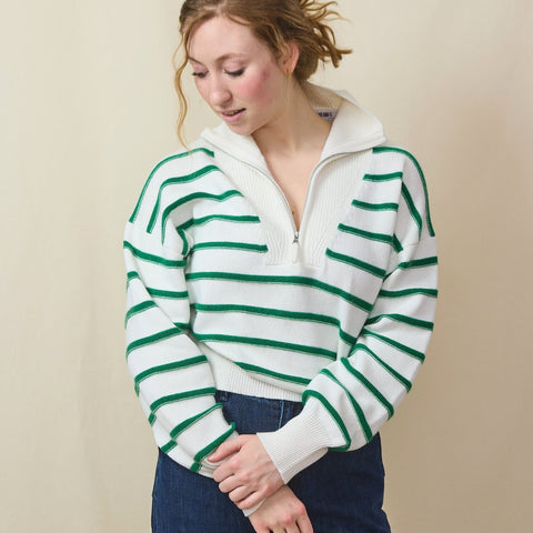 Tall blond woman wears a striped cotton/cashmere ¼ zip sweater and dark high waited jeans.