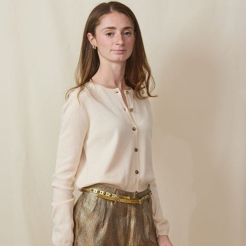 tall young woman wears a cream cotton/cashmere cardigan and gold bermuda shorts.